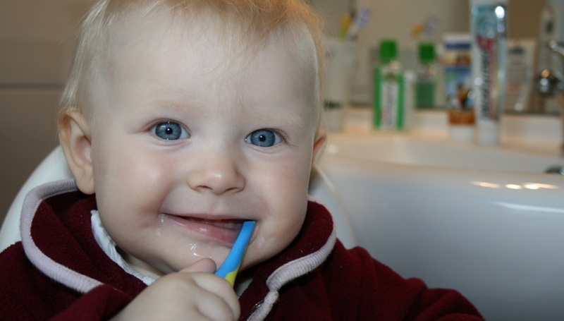 criança de olhos azuis a lavar os dentes com uma escova azul